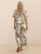 woman wearing loose fit floral print Meadow loose fit co-ord set with short sleeves and wide-leg trousers standing against beige background