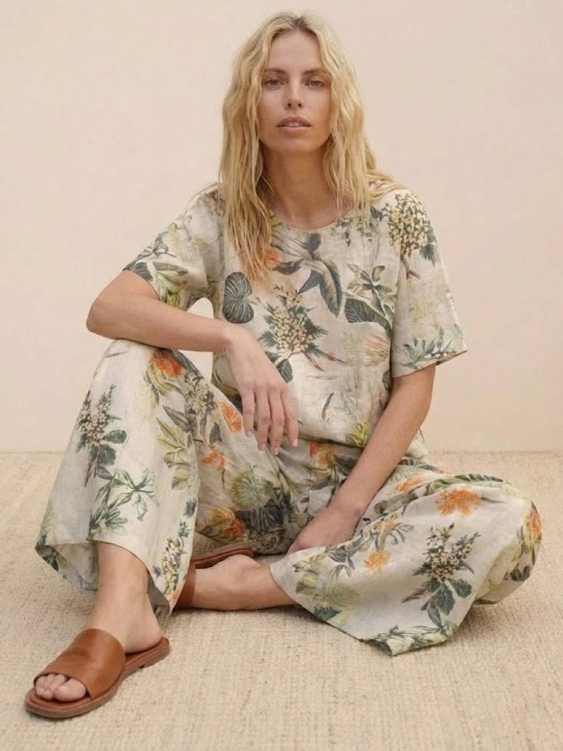 woman wearing floral loose fit co-ord set with wide-leg pants and short-sleeve top sitting on floor with brown sandals