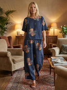Woman wearing a navy loose fit co-ord set with floral print, featuring a relaxed top and wide-leg trousers in a cozy living room setting