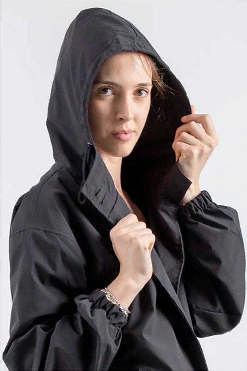 Woman wearing black Rain Couture Windbreaker with hood up, lightweight and water-resistant jacket.