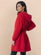 Woman wearing red Rain Couture Windbreaker with hood, oversized fit, and adjustable waist on beige background
