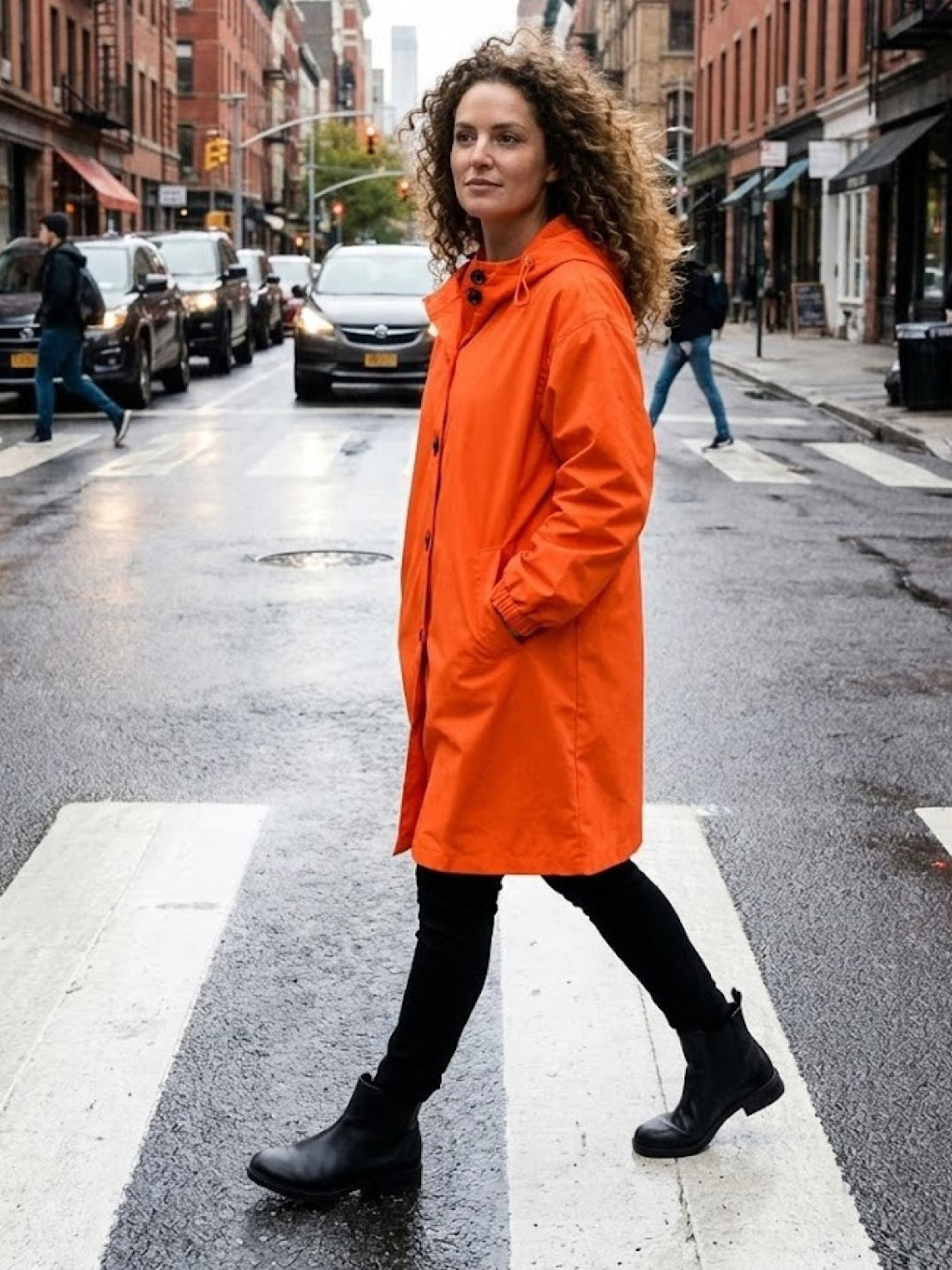 Woman wearing orange Rain Couture Windbreaker walking on a city street crosswalk