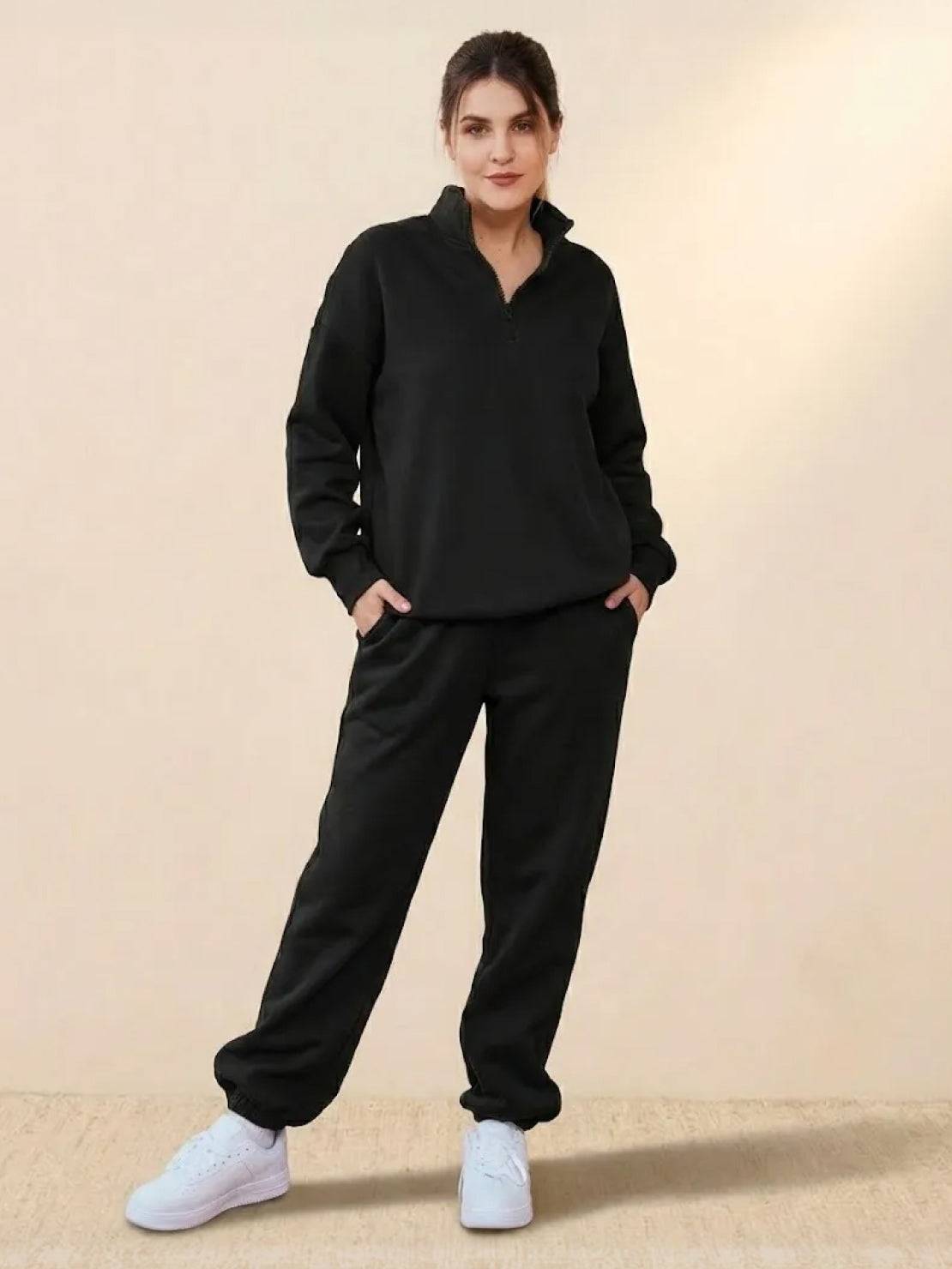 Woman wearing black ultra-soft and comfy co-ord tracksuit set with white sneakers standing against a beige background