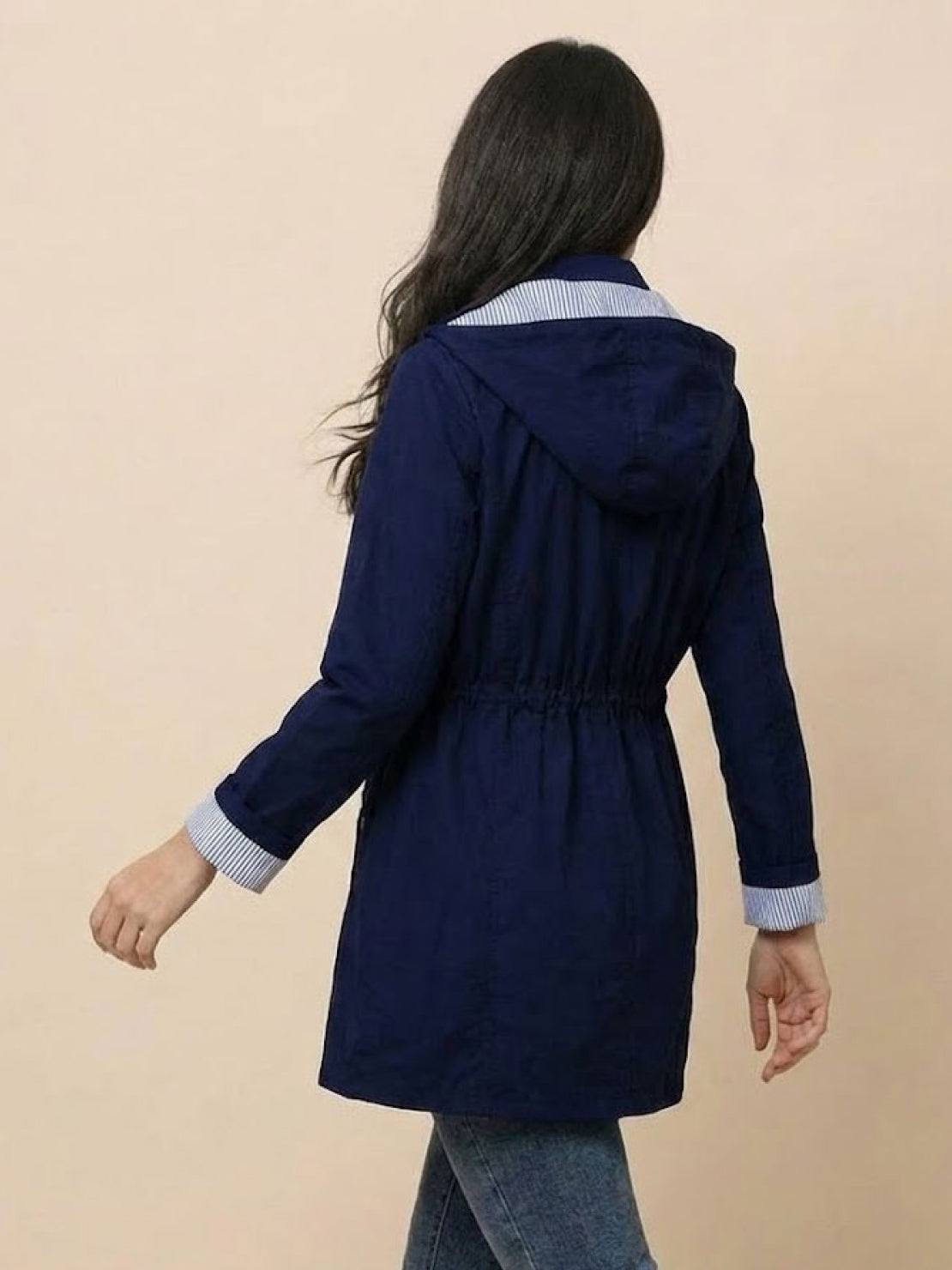 Woman wearing navy blue water resistant hooded windbreaker jacket with striped inner collar and cuffs, back view