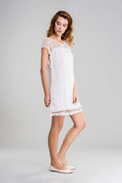 White pom pom lace mini dress with transparent shoulder panel and sleeveless design worn by model in neutral background