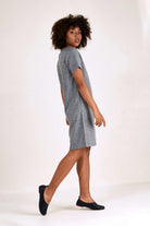 Woman wearing a grey short sleeve shift dress with round neck and side pockets, knee-length style